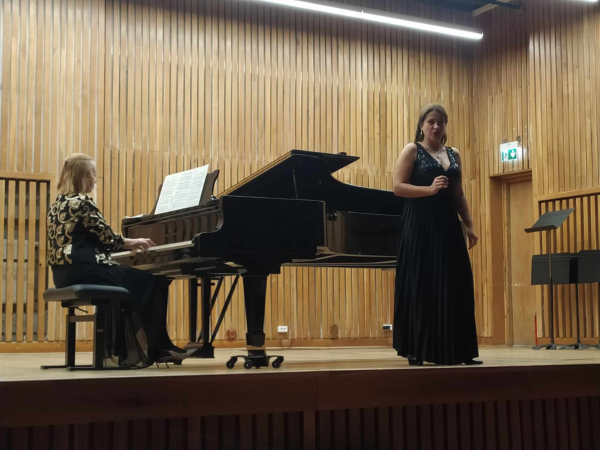 Kobieta gra na fortepianie, druga kobieta śpiewa.