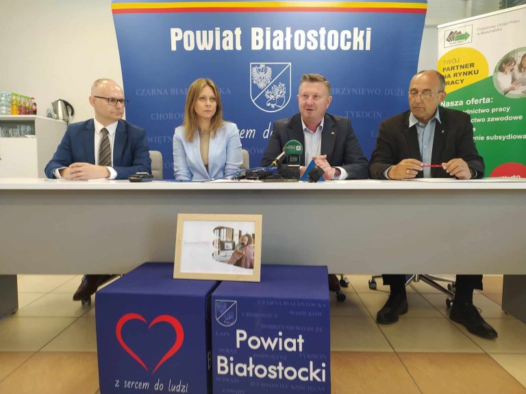 4 osoby siedzą za stołem przed mikrofonami.
