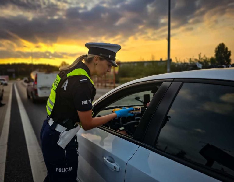 Policjantka trzyma alkomat, do którego dmucha kierowca siedzący w aucie.