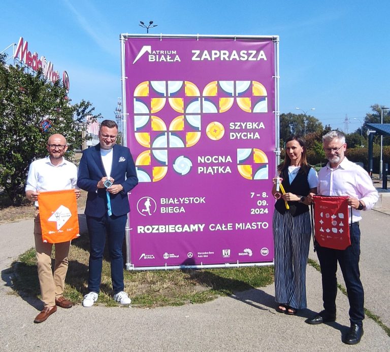 Organizatorzy i sponsorzy imprezy Białystok Biega, pozują z medalami przy grafice promującej wydarzenie