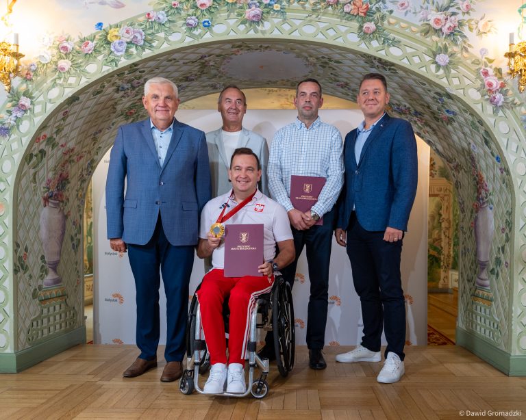 Mężczyźni, w tym jeden na wózku inwalidzkim, pozują do zdjęcia.