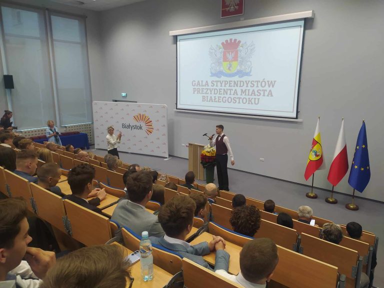 Na auli siedzą ludzie, a przed nim mężczyzna śpiewa do mikrofonu.