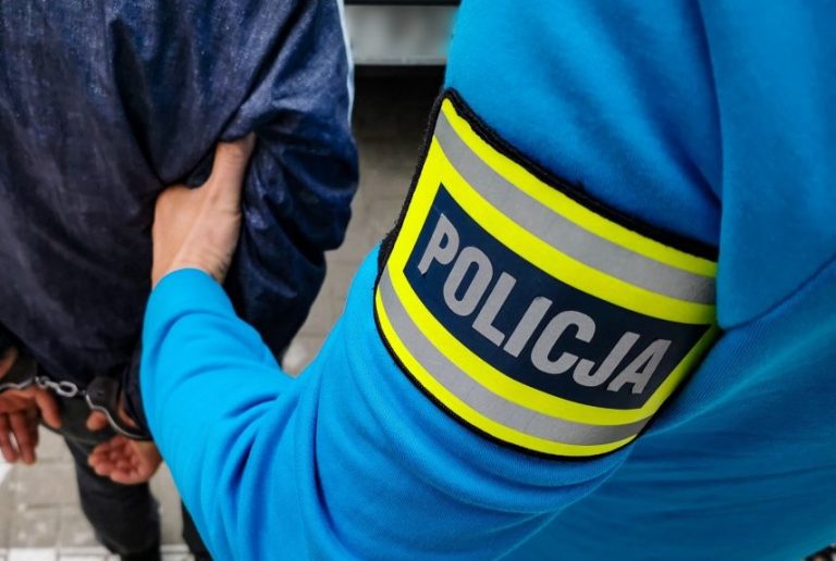 Ręka policja trzyma mężczyznę w kajdankach.