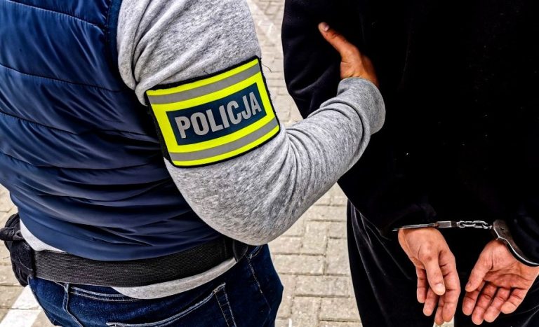 Mężczyzna z założonymi kajdankami, jest prowadzony przez policjanta