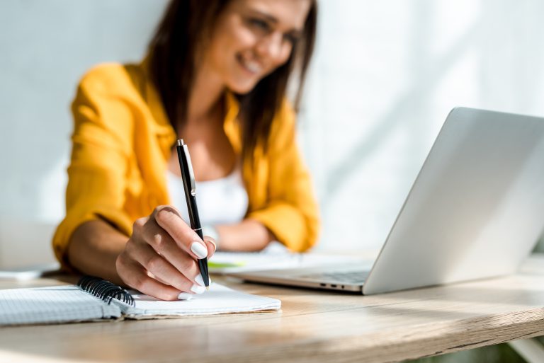 selective focus of freelancer writing and working with laptop in home office