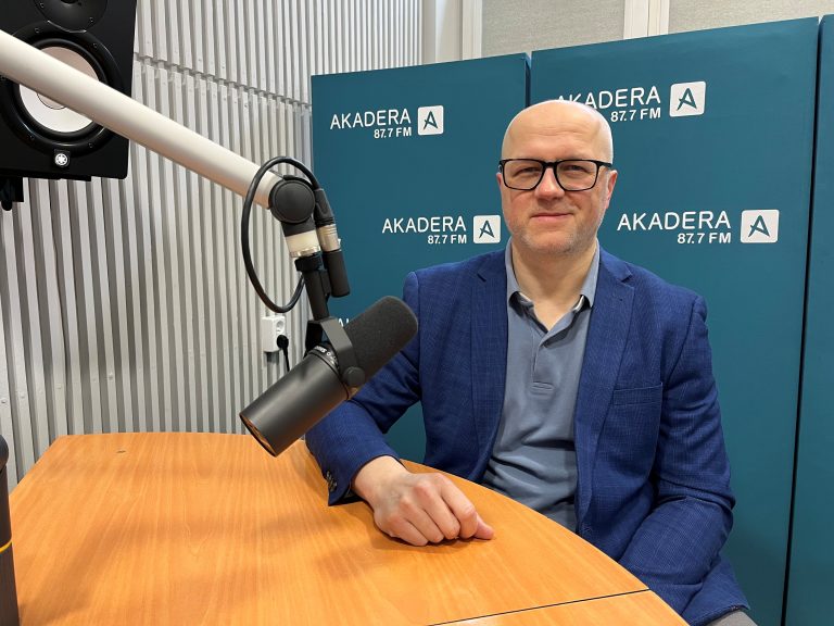 Dr inż. Paweł Tadejko siedzi przy mikrofonie w studiu Radia Akadera. W tle niebieskie ścianki z logo „AKADERA 87.7 FM”. Ma na sobie niebieską marynarkę i okulary.