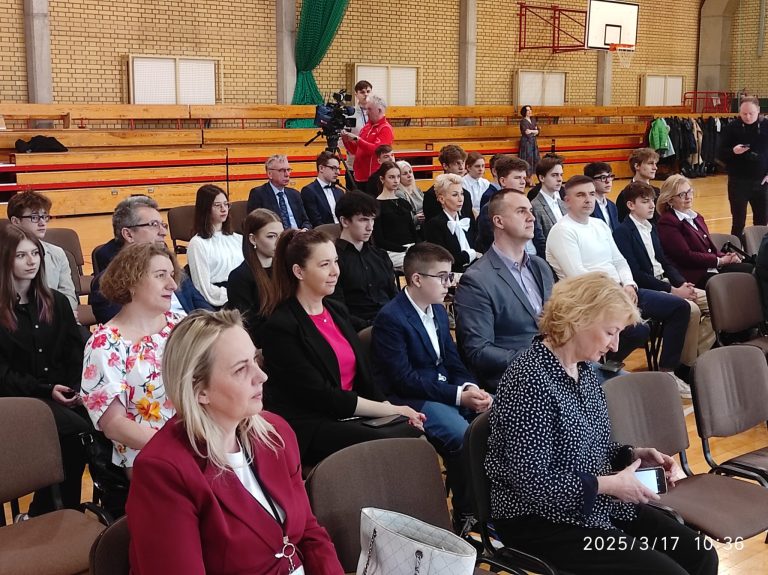Uczestnicy uroczystości siedzą na sali gimnastycznej