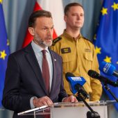 Mężczyzna w garniturze i strażak na konferencji prasowej.
