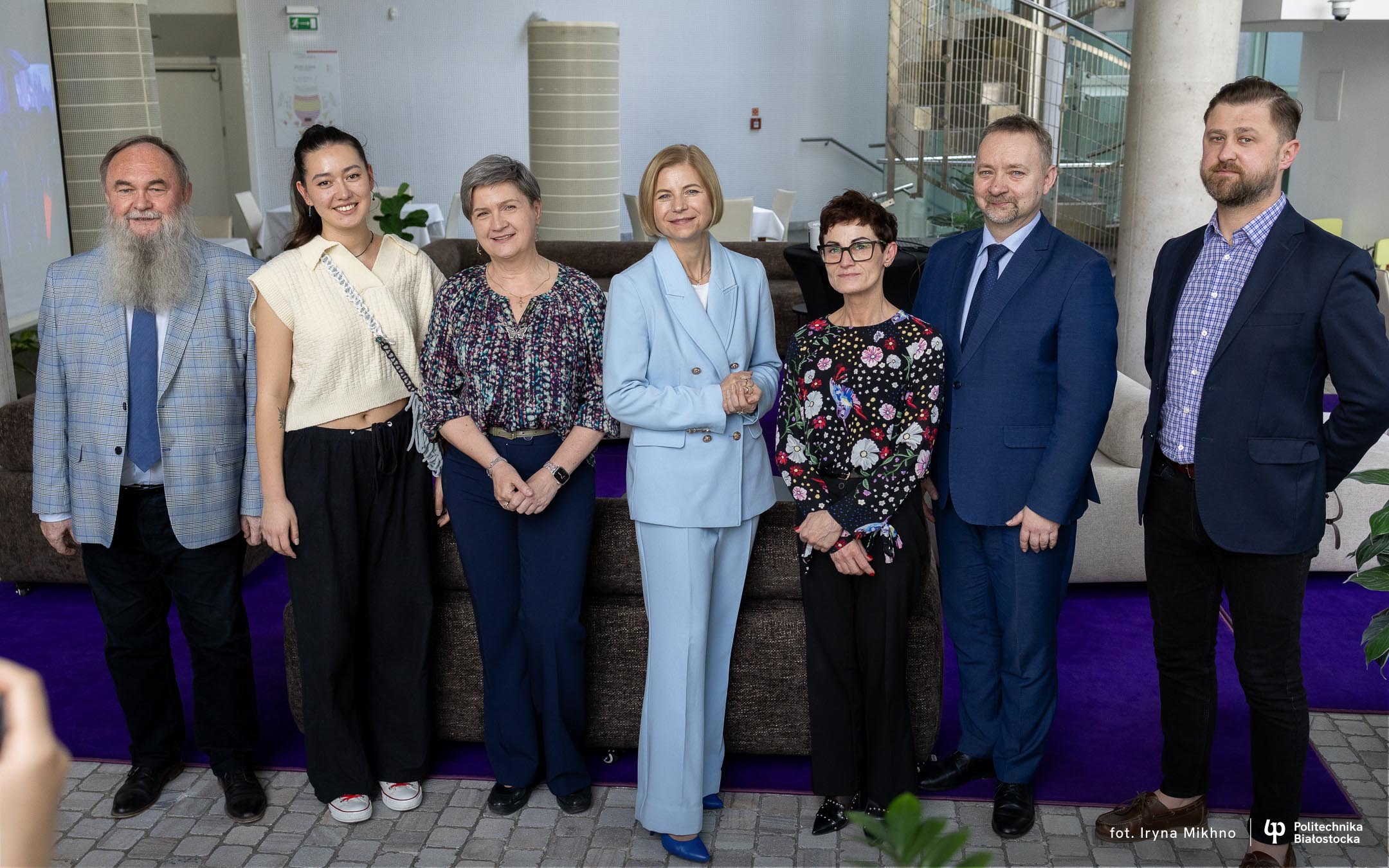 Grupa siedmiu partnerów kampanii „Nie wysiadaj w połowie drogi” pozuje wspólnie do zdjęcia podczas inauguracji akcji w Operze i Filharmonii Podlaskiej. Uśmiechnięci uczestnicy – kobiety i mężczyźni – reprezentują różne instytucje zaangażowane w działania na rzecz zdrowia psychicznego. W tle nowoczesne wnętrze z fioletowym dywanem i spiralnymi schodami.