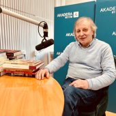 Andrzej Kalinowski, organizator Targów Książki w Białymstoku, siedzi przy stole w radiowym studiu Radia Akadera. Przed nim mikrofon oraz stos kolorowych książek. W tle niebieskie ścianki z logo Akadera 87.7 FM.