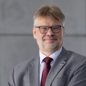 Zdjęcie przedstawia uśmiechniętego mężczyznę w okularach, w garniturze z czerwonym krawatem. Tło jest jednolite, szare. Na zdjęciu znajduje się dr hab. inż. Andrzej Gajewski.