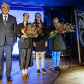 Prezydent Białegostoku Tadeusz Truskolaski oraz laureatki Nagrody Literackiej Kazaneckiego 2025 stoją na scenie z bukietami kwiatów, na tle niebieskiego światła i dekoracji.