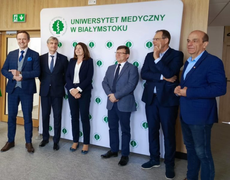 Na tle ścianki z napisem Uniwersytet Medyczny w Białymstoku, stoją elegancko ubrani ludzie, podczas konferencji prasowej. Na zdjęciu m.in. Rektor UMB w Białymstoku oraz Pani Dyrektor UDSK w Białymstoku.