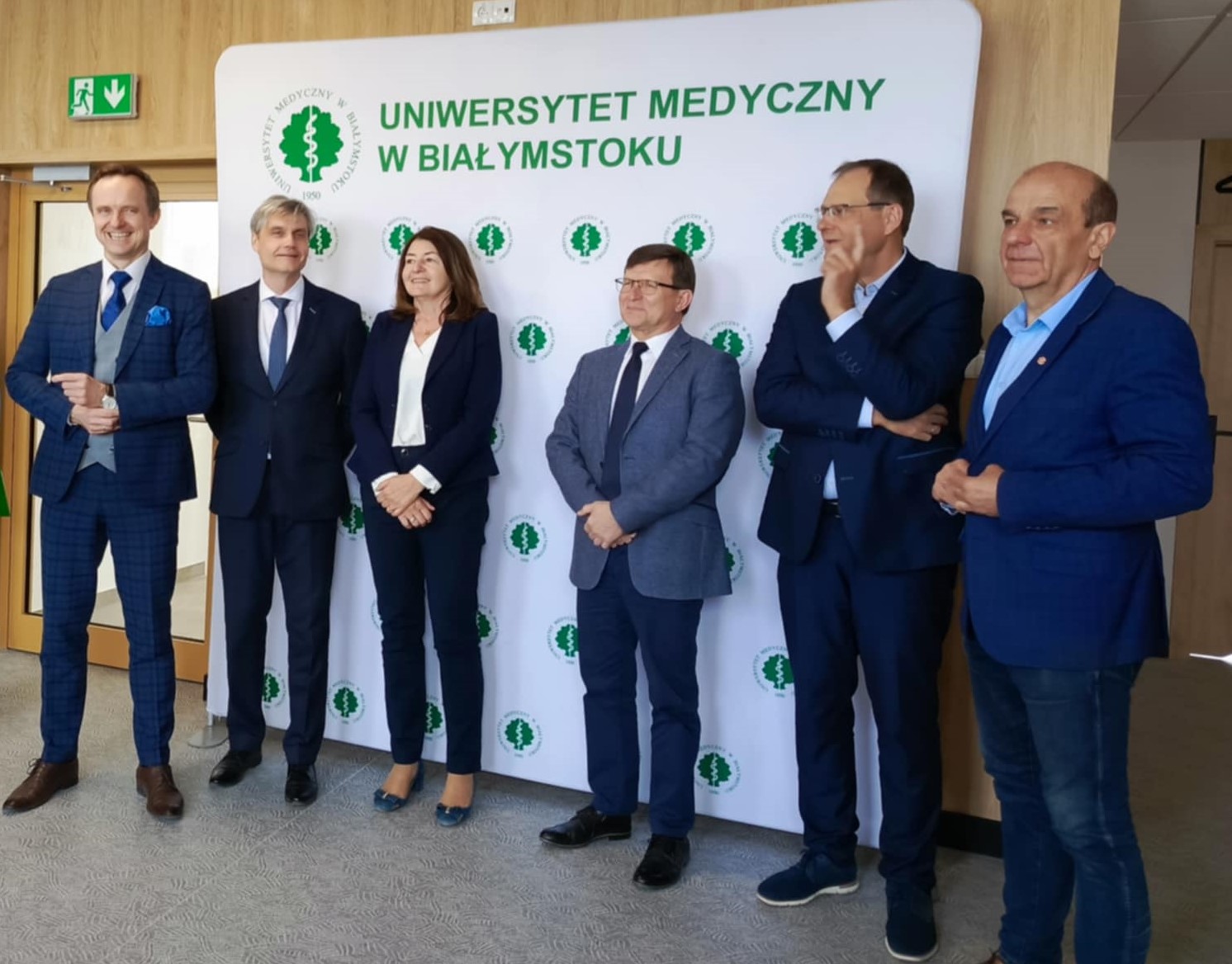 Na tle ścianki z napisem Uniwersytet Medyczny w Białymstoku, stoją elegancko ubrani ludzie, podczas konferencji prasowej. Na zdjęciu m.in. Rektor UMB w Białymstoku oraz Pani Dyrektor UDSK w Białymstoku.