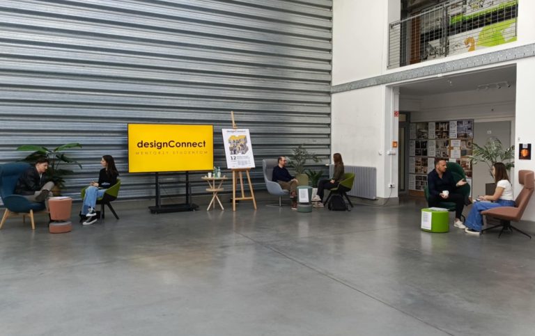 Na zdjęciu hala na Wydziale Architektury PB, na niej duzy ekran z napisem na żółtym tle DESIGN CONNECT. Przy stolikach siedzą mentorzy oraz studenci, trwają rozmowy i porady.