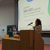 Kobieta na mównicy przemawia na tle wyświetlanego napisu z tematyka konferencji
