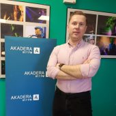 Na zdjeciu mezczyzna ubrany w rozowa koszule, elegancki, na tle niebieskiej planszy Radio Akadera i zdjec zespolow na koncertach.