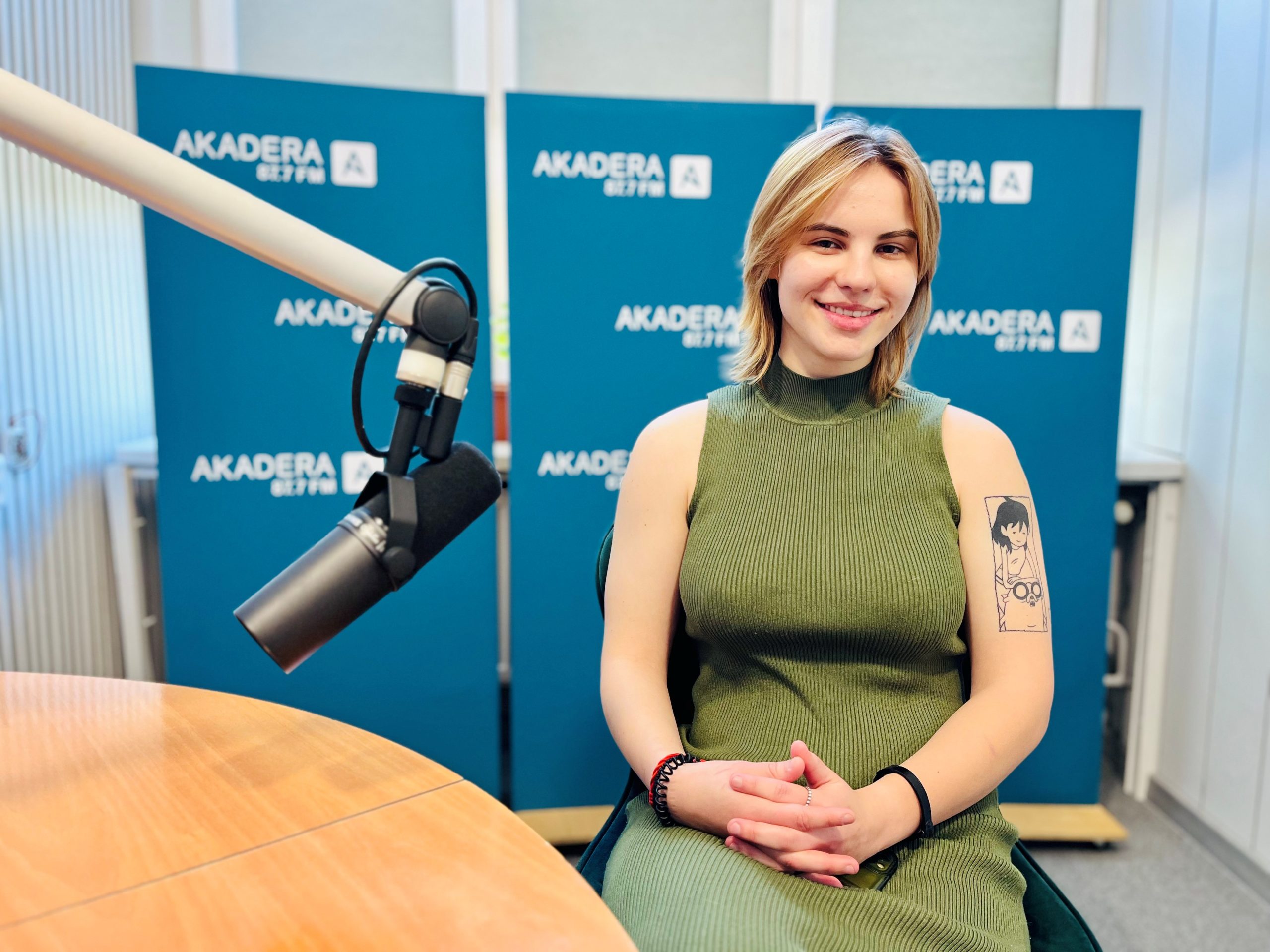 Uśmiechnięta Aleksandra Hackiewicz, studentka leśnictwa z Politechniki Białostockiej, siedzi przy mikrofonie w studiu Radia Akadera. Ma na sobie zieloną, bezrękawną sukienkę i widoczny tatuaż z postacią anime na lewym ramieniu. W tle plansze z logo Radia Akadera 87,7 FM.