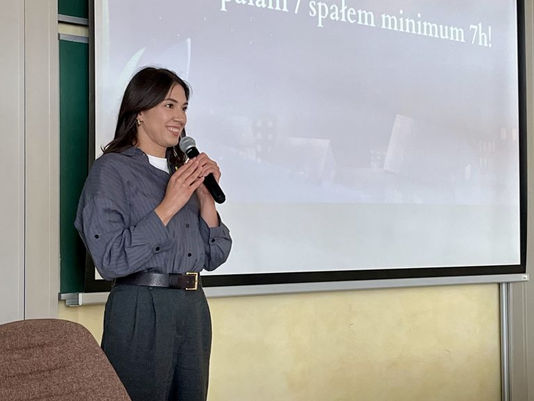 Daria Łukowska prowadzi wykład na Politechnice Białostockiej. Stoi z mikrofonem przed ekranem, na którym wyświetlony jest slajd z napisem „1/3 życia 'tracisz' na sen”.