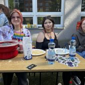 Trzy studentki Wydziału Architektury PB siedzące przy stole z watą cukrową i przekąskami, uśmiechnięte i ubrane kolorowo.