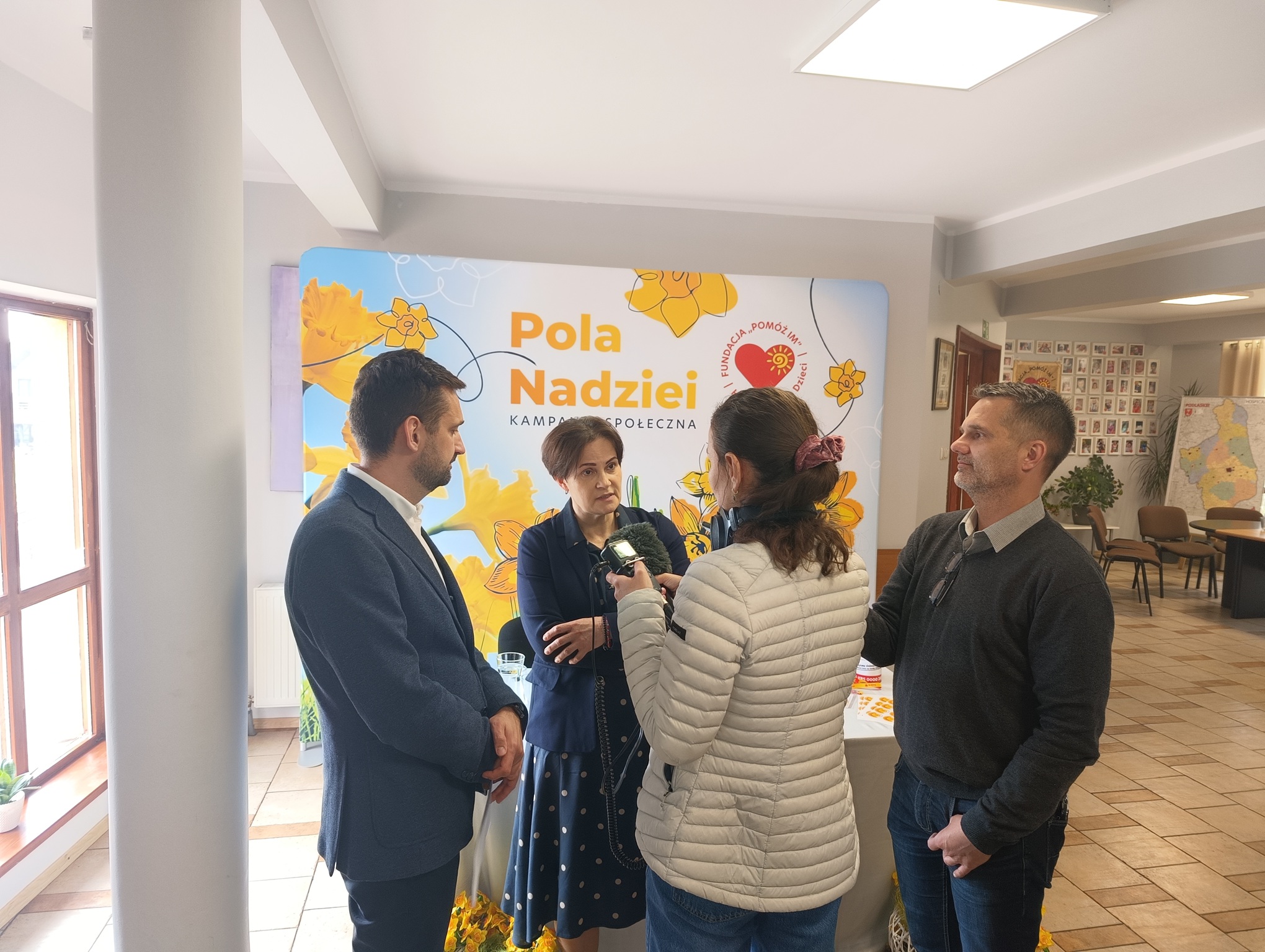 Joanna Czupryńska-Kwiatkowska i Eryk Latocha z Fundacji „Pomóż Im” udzielają wywiadu mediom podczas konferencji prasowej kampanii „Pola Nadziei”. W tle ścianka z logo kampanii i żonkilami.