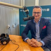 Wiceprezydent Rafał Rudnicki siedzi przy mikrofonie w studiu Radia Akadera; ma granatową marynarkę, koszulę w niebiesko-białe pasy i czerwony poszetka, przed nim leżą studyjne słuchawki.