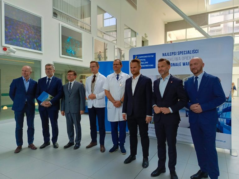 mezczyzni stoja na tle scianki z napisem Uniwersytecki Kliniczny Szpital