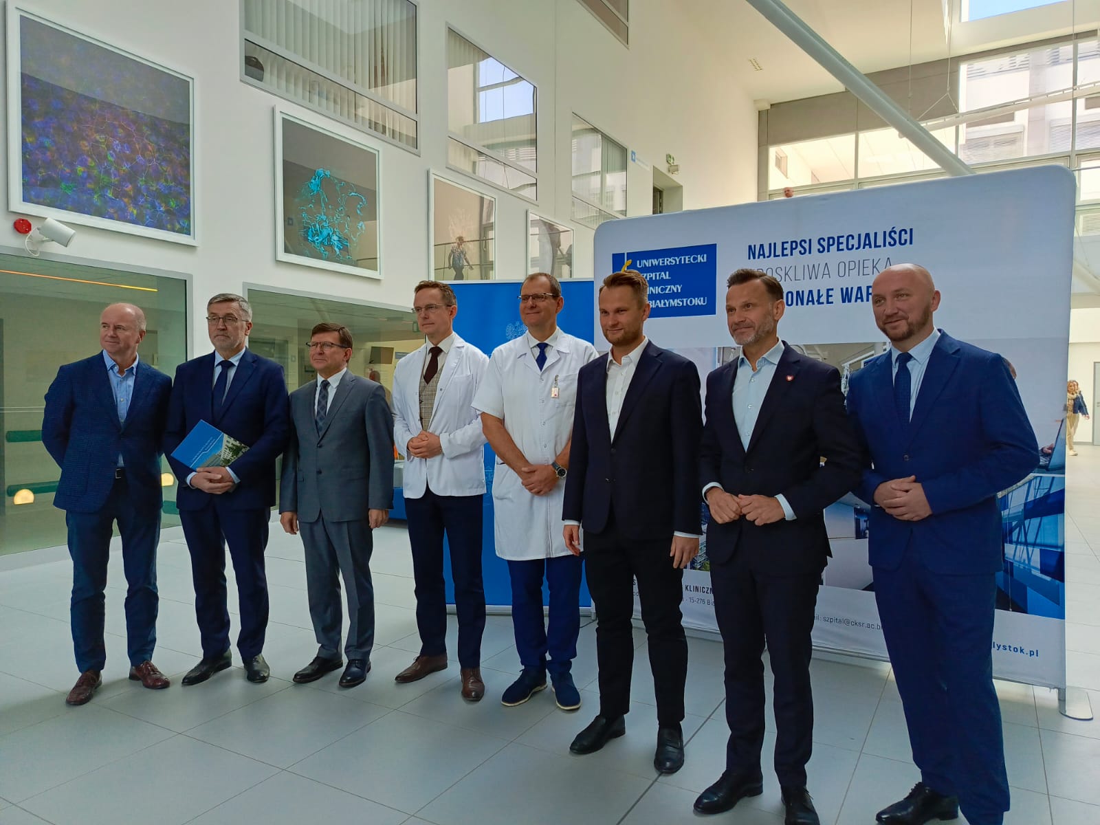 mezczyzni stoja na tle scianki z napisem Uniwersytecki Kliniczny Szpital