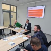 Prowadzący panel siedzą przy laptopie, w tle ekran z planszą „Akcja kwaterowanie” i punktami dotyczącymi zakwaterowania studentów
