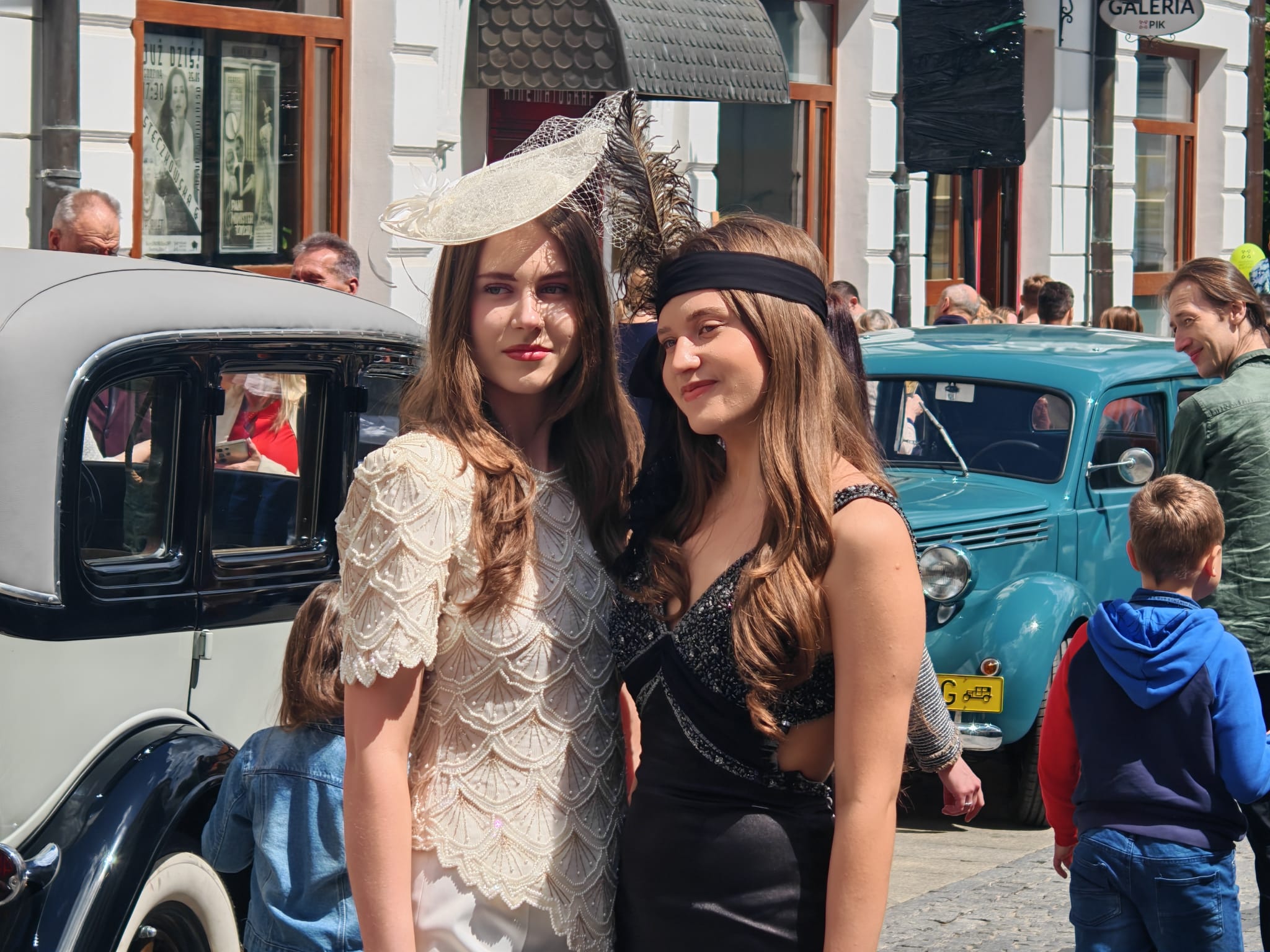 Modelki w stylizacjach na lata 20. i 30. XX wieku, pozują na tle retro aut.