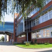 Widok na przeszklony budynek wydziału Politechniki Białostockiej z czerwonej cegły, z alejką i spacerującymi studentami