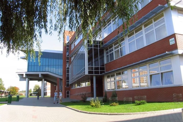 Widok na przeszklony budynek wydziału Politechniki Białostockiej z czerwonej cegły, z alejką i spacerującymi studentami