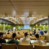 SALA WYKLADOWA SIEDZA STUDENCI W LAWKACH NA DOLE WYSWIETLACZ Z INFORMACJAMI O KONFERENCJI BEZPIECZENSTWO W BUDOWNICTWIE