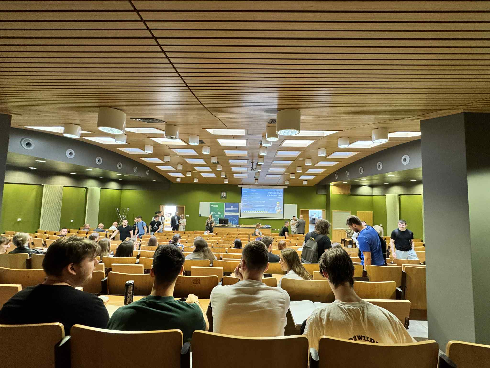 SALA WYKLADOWA SIEDZA STUDENCI W LAWKACH NA DOLE WYSWIETLACZ Z INFORMACJAMI O KONFERENCJI BEZPIECZENSTWO W BUDOWNICTWIE