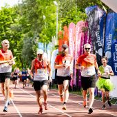 sportowcy biegna w biegu ekiden wsrod zieleni drzew w tle flagi z imprezy