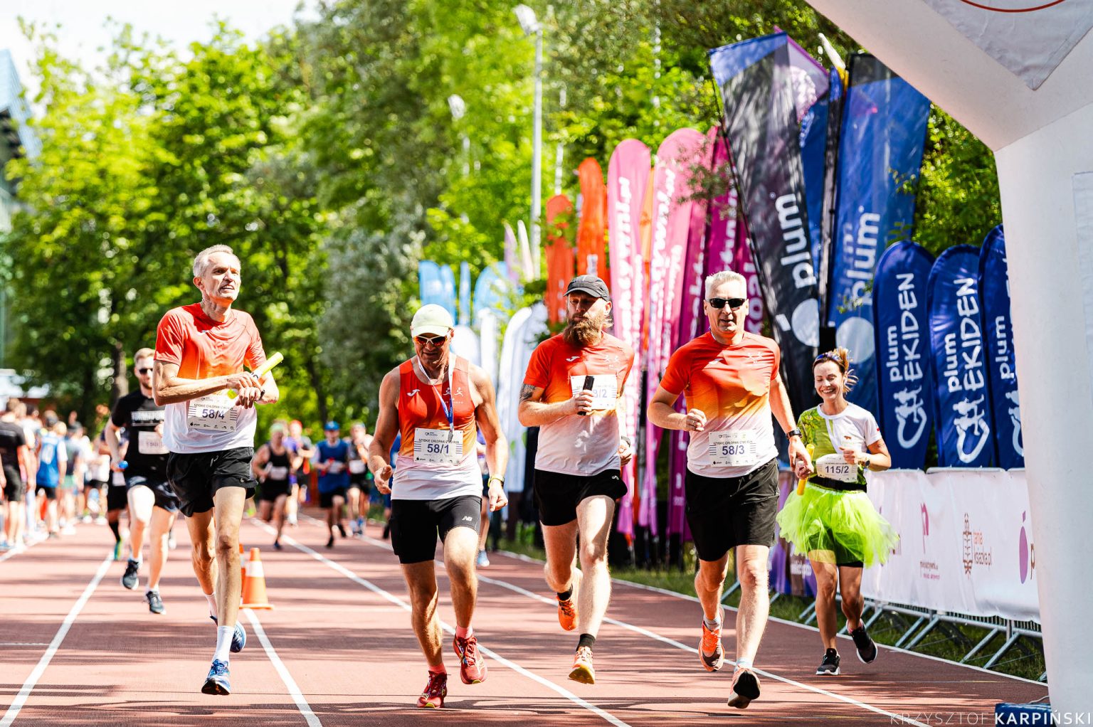 sportowcy biegna w biegu ekiden wsrod zieleni drzew w tle flagi z imprezy
