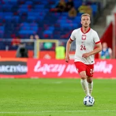 Mateusz Skrzypczak biegnie z piłką po zielonej murawie, nosi białą koszulkę reprezentacji Polski