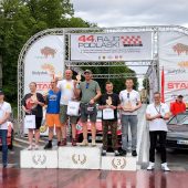 Zwycięzcy 44. Rajdu Podlaskiego stoją na podium podczas ceremonii wręczenia nagród na placu NZS w Białymstoku. W tle baner z logo rajdu oraz sponsorami wydarzenia.