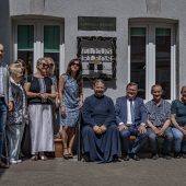 Grupa osób, w tym duchowni, samorządowcy i pracownicy Eleos, pozuje do wspólnego zdjęcia na tle budynku Prawosławnego Ośrodka Miłosierdzia Eleos w Białymstoku. Pośrodku widoczny szyld z napisem „Ławeczka Nadziei” oraz stylizowane metalowe logo Eleos.