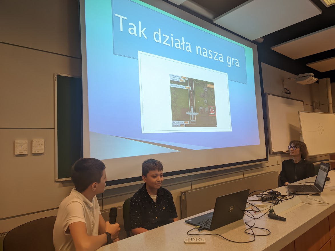 Uczniowie prezentują grę na telebimie.
