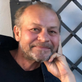 Wojciech Szelachowski uśmiechnięty siwa broda ręką podpiera podbródek