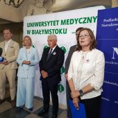 Na zdjęciu widzimy konferencję prasową zorganizowaną wspólnie przez Uniwersytet Medyczny w Białymstoku oraz Podlaski Oddział Narodowego Funduszu Zdrowia. Przed ściankami z logotypami instytucji stoją przedstawiciele organizatorów, m.in. kobieta w białej bluzce, mężczyzna w jasnym garniturze oraz kobieta w błękitnym garniturze. Wszyscy mają przypięte identyfikatory z grafiką kampanii zdrowotnej, co sugeruje, że wydarzenie dotyczyło profilaktyki, edukacji zdrowotnej lub ogólnopolskiego programu badań. Przed uczestnikami ustawiony jest mikrofon TVP3 Białystok, co wskazuje na obecność mediów.