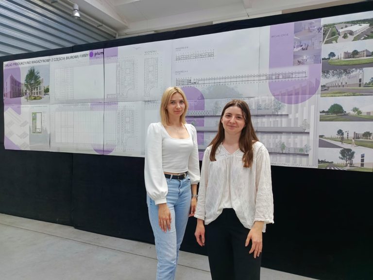 Na zdjęciu widzimy dwie studentki Wydziału Architektury Politechniki Białostockiej stojące przed planszą prezentującą ich projekt koncepcyjny zakładu produkcyjno-magazynowego z częścią biurową dla firmy PLUM. Wizualizacje, rysunki techniczne i układ funkcjonalny zaprezentowane na planszy świadczą o profesjonalnym podejściu i wysokim poziomie przygotowania projektu. Autorkami pracy są Dominika Dylewicz i Urszula Łukaszuk – laureatki konkursu ogłoszonego przez firmę PLUM.