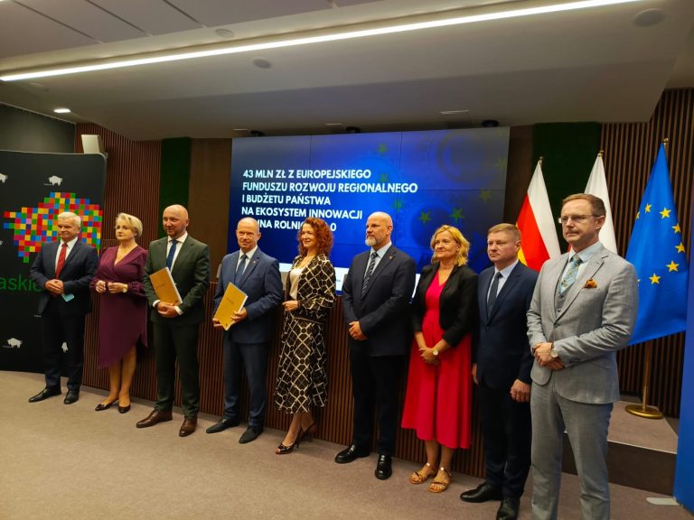 Na zdjęciu widzimy prof. Martę Kosior-Kazberuk, rektor Politechniki Białostockiej, podczas wydarzenia związanego z podpisaniem umowy na dofinansowanie projektu „Ekosystem Innowacji Dolina Rolnicza 4.0”. Za rektorką znajduje się ekran informujący o przyznaniu 43 mln zł z Europejskiego Funduszu Rozwoju Regionalnego i budżetu państwa na realizację tego strategicznego przedsięwzięcia. Projekt ma na celu integrację nauki, nowoczesnych technologii i biznesu w sektorze rolnictwa oraz przetwórstwa rolno-spożywczego.