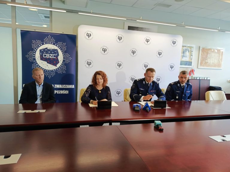 rektor pb i mezczyzni w mundurze podpisuja porozumienie na tle scianki