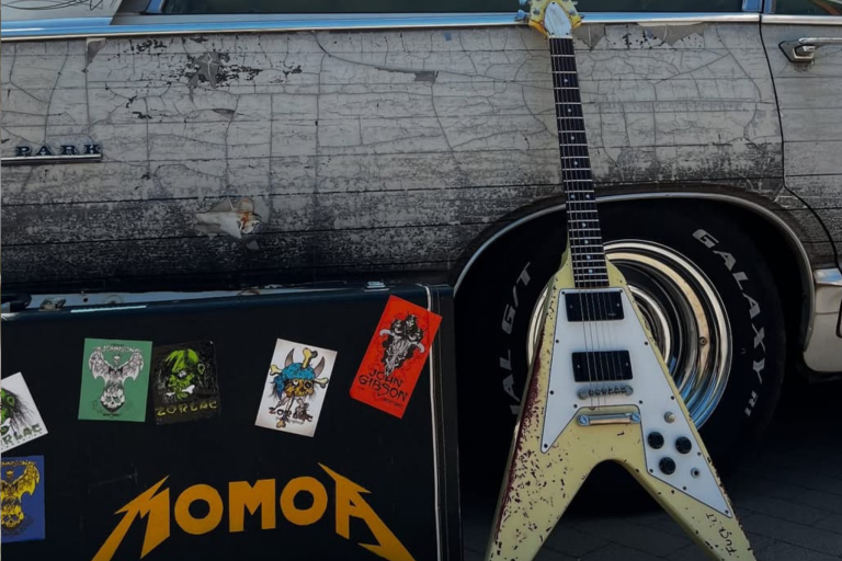 Gitara typu Flying V – klasyczny model Gibsona, który pokochali tacy giganci jak Jimi Hendrix, K.K. Downing (Judas Priest) czy Michael Schenker. Jej zużyty wygląd świadczy, że wiele przeszła – prawdziwy wojownik sceniczny!