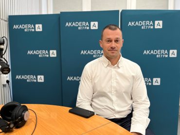 Paweł Orpik, dyrektor BOSiR, siedzi przy stole w studiu Radia Akadera 87,7 FM, ubrany w białą koszulę, w tle niebieskie ścianki z logo stacji.