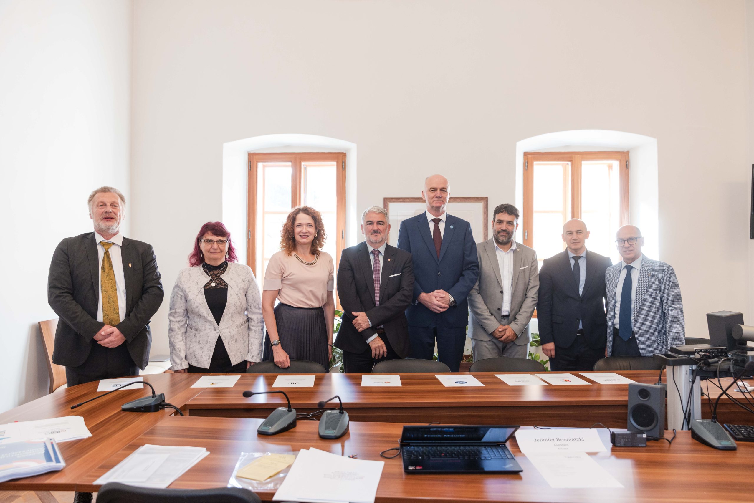 Grupa rektorów i przedstawicieli uczelni partnerskich Uniwersytetu Europejskiego ACROSS stoi wspólnie w sali konferencyjnej podczas uroczystego podpisania umowy konsorcjum w Nowej Goricy.