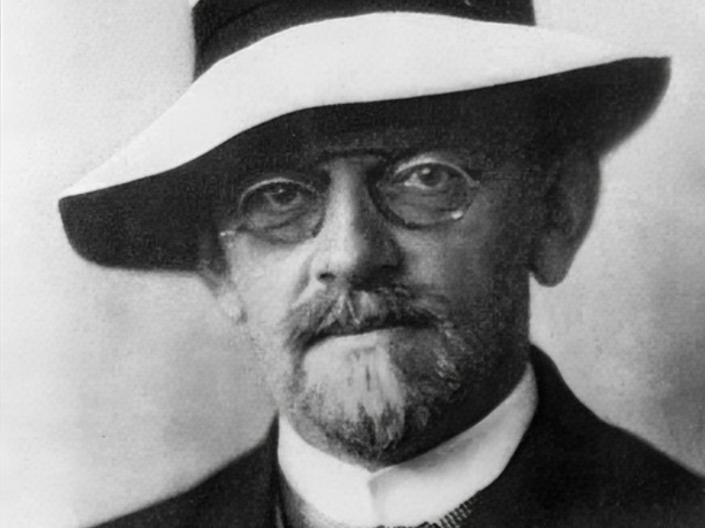 Czarno-biała fotografia Davida Hilberta w eleganckim kapeluszu i okrągłych okularach, ukazująca uczonego w średnim wieku, z brodą i poważnym wyrazem twarzy.