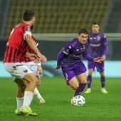 Piłkarz Jagiellonii Białystok w fioletowym stroju prowadzi piłkę podczas meczu ze Shkendiją Tetowo w Lidze Konferencji Europy. W tle widać zawodników obu drużyn na murawie stadionu w Skopje.